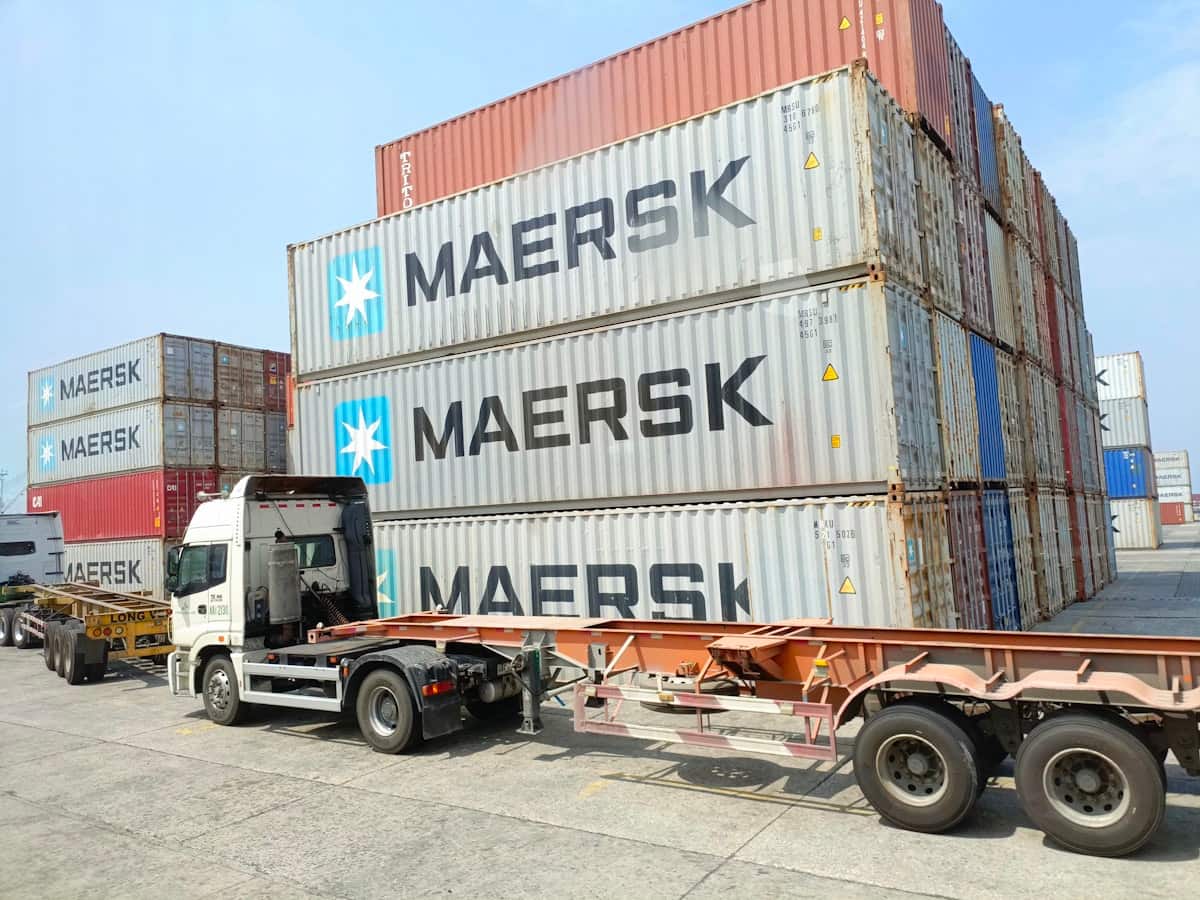A drayage tractor coupled to a container chassis on the apron inside Manila port terminal, with stacked Maersk containers rising behind it.
