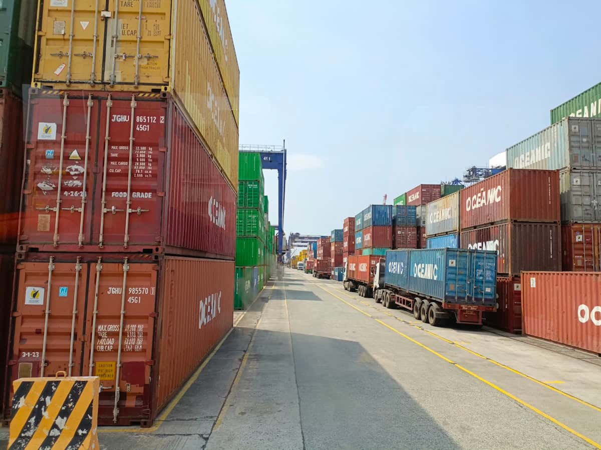 An empty service lane running between two walls of weathered stacked containers at Manila South Harbor, a line of parked chassis receding into the distance under a pale sky.